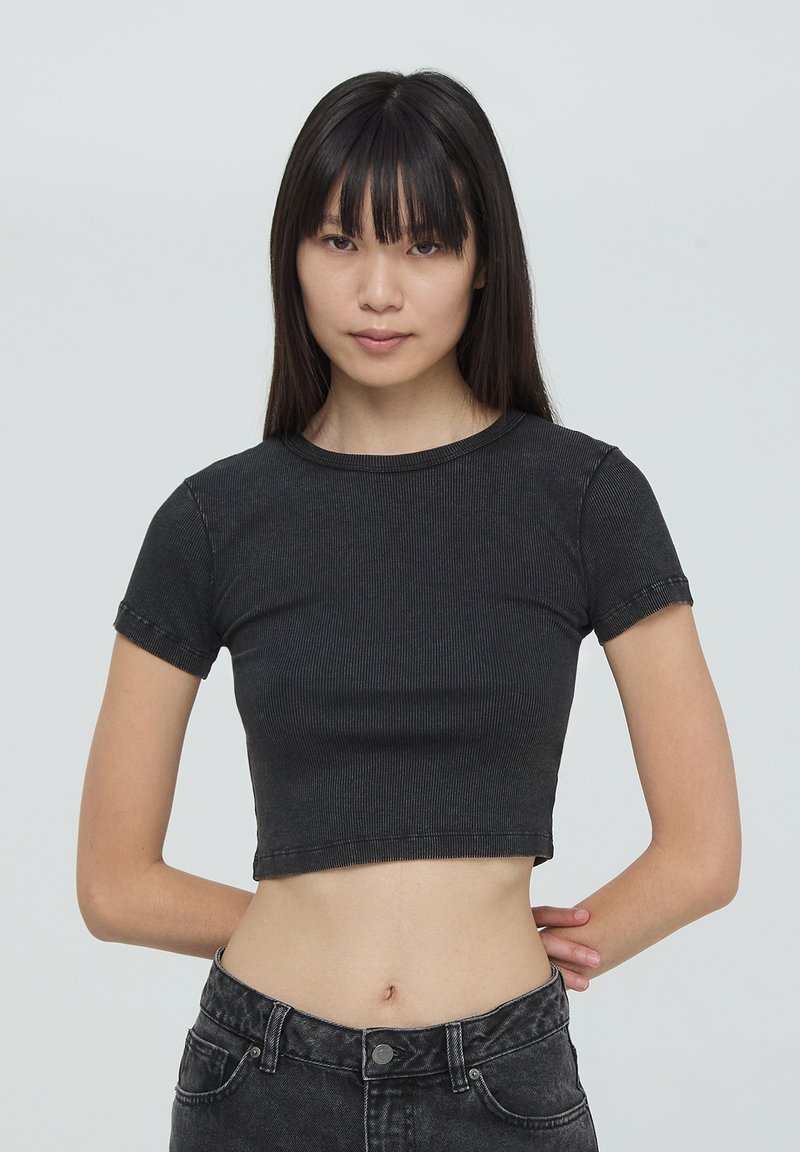 T-shirt nera cropped realizzata in tessuto a coste, con maniche corte e scollo rotondo. Presenta un design aderente e cuciture visibili.