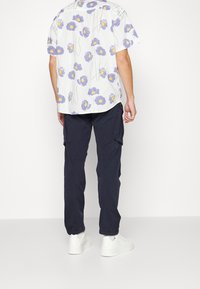 Kortärmad skjorta med blommor i lila och gröna stjälkar på en ljus bakgrund, tillsammans med mörka cargo-byxor och vita sneakers.