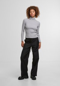 Szary sweter z golfem o prążkowanej fakturze z długimi rękawami, zestawiony z czarnymi spodniami dresowymi na sznurki i masywnymi czarnymi butami na platformie.