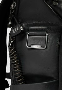 Zwart leren interieur van een tas met zilverkleurige metalen bevestiging, een combinatieslot en een spiraalvormige ritssluiting voor extra beveiliging.