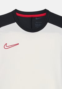 Camiseta deportiva Dri-FIT blanca con mangas negras y un acento de cuello rojo, con un logotipo de Nike bordado en rojo en la parte frontal.