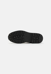 Suela de zapato de goma negra con un patrón de banda de rodadura robusto, que presenta surcos verticales y horizontales para tracción. Texto/logo en relieve en la superficie.