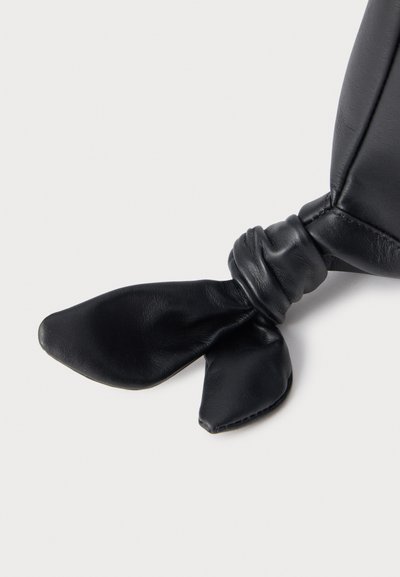 Gant en cuir noir avec un gros nœud lâche noué au poignet, présenté sur un fond clair uni.