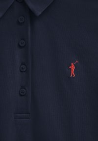 Marineblaues Poloshirt aus strukturiertem Stoff, mit fünf dunklen Knöpfen und einer kleinen roten gestickten Figur, die einen Golfschläger hält.