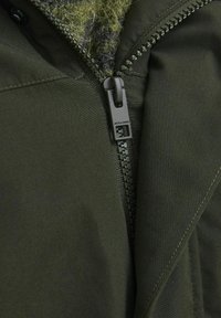 Olive green jacket with a textured inner lining and a zipper closure featuring a branded pull tab. Smooth fabric with stitching details.