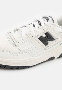 White leather sneaker with perforated detailing, prominent black "N" logo, and textured black rubber sole. Features laces and subtle gray accents.