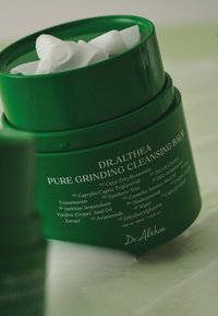 Zielony słoik balsamu oczyszczającego Dr. Althea Pure Grinding z białą, teksturowaną wewnętrzną pokrywą oraz szczegółami składników wydrukowanymi na boku w białym kolorze.