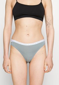 Lacoste ljusgrå tanga med en vit midja som har en logotyp. Materialet är mjukt, stretchigt, med en slät textur och minimalistisk design.