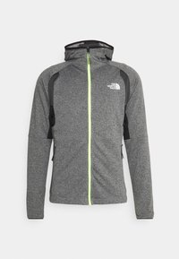 Giacca grigia con una finitura testurizzata, dettagli neri, zip completa e cappuccio. Presenta una zip e un logo verde neon sulla parte sinistra del petto.