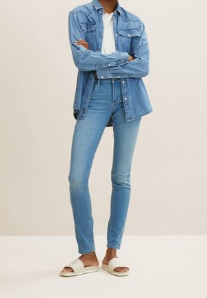 Camisa de mezclilla de botones en azul claro, llevada sobre una camiseta blanca de canalé; combinada con jeans de talle alto azules y sandalias blancas de cuadro.