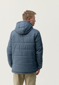 Podložena jakna s kapuco v umirjeni modri barvi, ki ima prešito zasnovo in elastične manšete. Gladka tekstura in srednja dolžina.