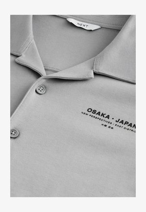 Szürke póló, puha anyagból, klasszikus gallérral és két gombbal. A mellkason található felirat: "OSAKA • JAPÁN."
