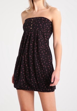 Strapless black mini dress with small pink anchor and floral patterns, button detail on front, worn by a person standing against a plain background.