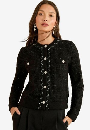 Schwarze strukturierte Strickjacke mit tailliertem Design, ausgestattet mit silbernen Knöpfen, zwei Vordertaschen und einem Rundhalsausschnitt.