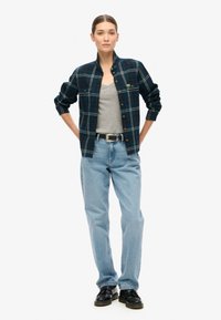 Camisa de franela en navy con cuadro verde y blanco, con un frente abotonado y mangas enrolladas, combinada con jeans rectos de lavado claro y zapatos negros.