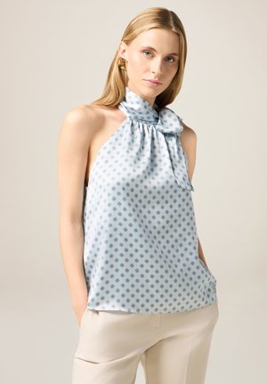 Top halter azzurro chiaro realizzato in tessuto liscio, con piccoli motivi a diamante e un dettaglio a fiocco al collo. Abbinato a pantaloni chiari.