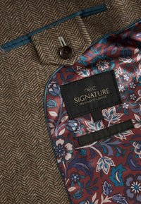 Brunt hørflet stof med blå satinkant, med en blomsterpræget burgunderforing og et sort mærke med teksten "next SIGNATURE PREMIUM TAILORING."