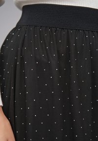 Sort tylskørt med en tekstureret elastisk linning, prydet med et mønster af små, skinnende prikker jævnt fordelt over stoffet.