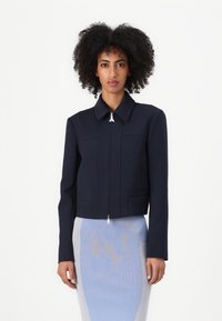 Marineblå cropped jakke med en strukturert design, med lange ermer, frontlommer og en sølvfarget glidelåsdetalj ved kragen.
