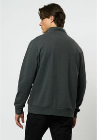 Sudadera gris oscuro con un cuello alto, mangas largas y puños y dobladillo acanalados. Textura suave, ajuste informal y diseño minimalista.