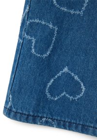 Tejido de denim de color azul con patrones en forma de corazón en azul claro. Los bordes están cosidos de manera prolija, con un ligero detalle deshilachado.