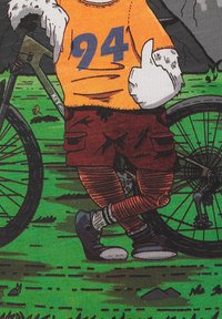 Persoon met een oranje shirt met het nummer "94" en rode cargoshorts, die een duim omhoog steekt terwijl hij naast een fiets op het gras staat.