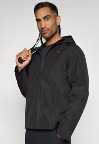 Mustan veekindla jope, millel on tõmblukk, reguleeritav kapuuts ja küljetaskud. Vasakul rinnal on väike punane logo.