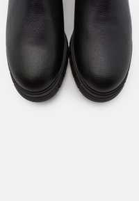Black leather ankle shoes with a textured finish, rounded toe, and thick rubber sole. Design is minimalist with no visible hardware or accents.