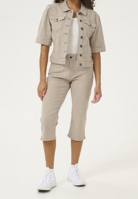 Beige corduroy cropped pants and matching jacket with short sleeves and button closure. White t-shirt underneath. White sneakers.