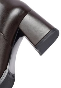 Brown leather high-heeled shoe featuring a chunky heel with a smooth, shiny surface. The design includes a rounded toe and a sleek profile.
