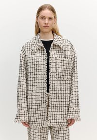 Tweed jasje in een crèmekleurig en zwart geruit patroon, met een franjeszoom, oversized pasvorm en grote kraag. G gedragen over een zwart top.