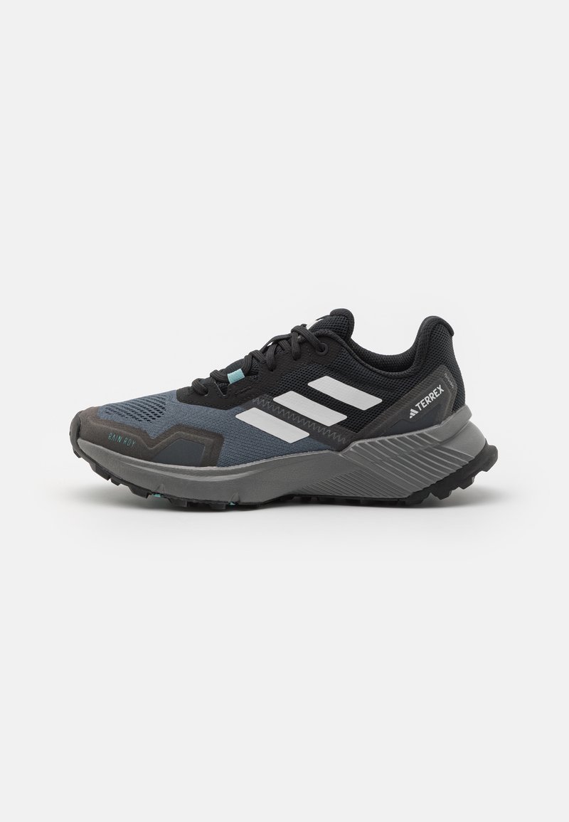 Zwarte en grijze sport schoen met een gestructureerde mesh bovenkant, witte strepen en een robuuste buitenzool ontworpen voor grip. Accenten met teal details.