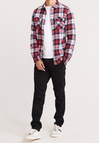 Rød og blå ternet flannel skjorte med to brystlommer, båret over en hvid t-shirt, parret med sorte bukser og hvide sneakers.