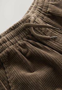 Primo piano di pantaloni di velluto a coste marroni con vita elastica e coulisse marrone coordinata.