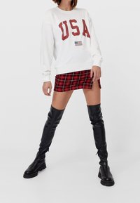 Sudadera blanca con "USA" en letras rojas y una pequeña bandera. Falda mini de cuadro rojo. Botas negras hasta la rodilla con suela gruesa y cremalleras.
