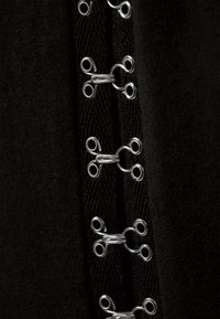 Tissu noir avec des œillets métalliques argentés verticaux et des embellissements en crochet. Le motif comprend des boucles alternées de tailles plus grandes et plus petites.