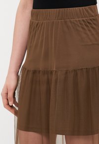 Brun tulle-skjørt med elastisk midjeband og lagdelt volangdesign, med en gjennomsiktig tekstur og glatt innerforing.