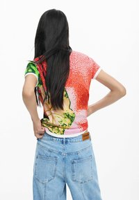 Rövid ujjú póló színes grafikai mintával, piros, zöld és sárga színekkel. Puha anyagból készült, kerek nyakkivágással és fehér szegéllyel.