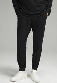Zwarte katoenen joggers met een elastische tailleband en trekkoord. Tapered leg ontwerp met geribde manchetten, gecombineerd met witte sneakers.