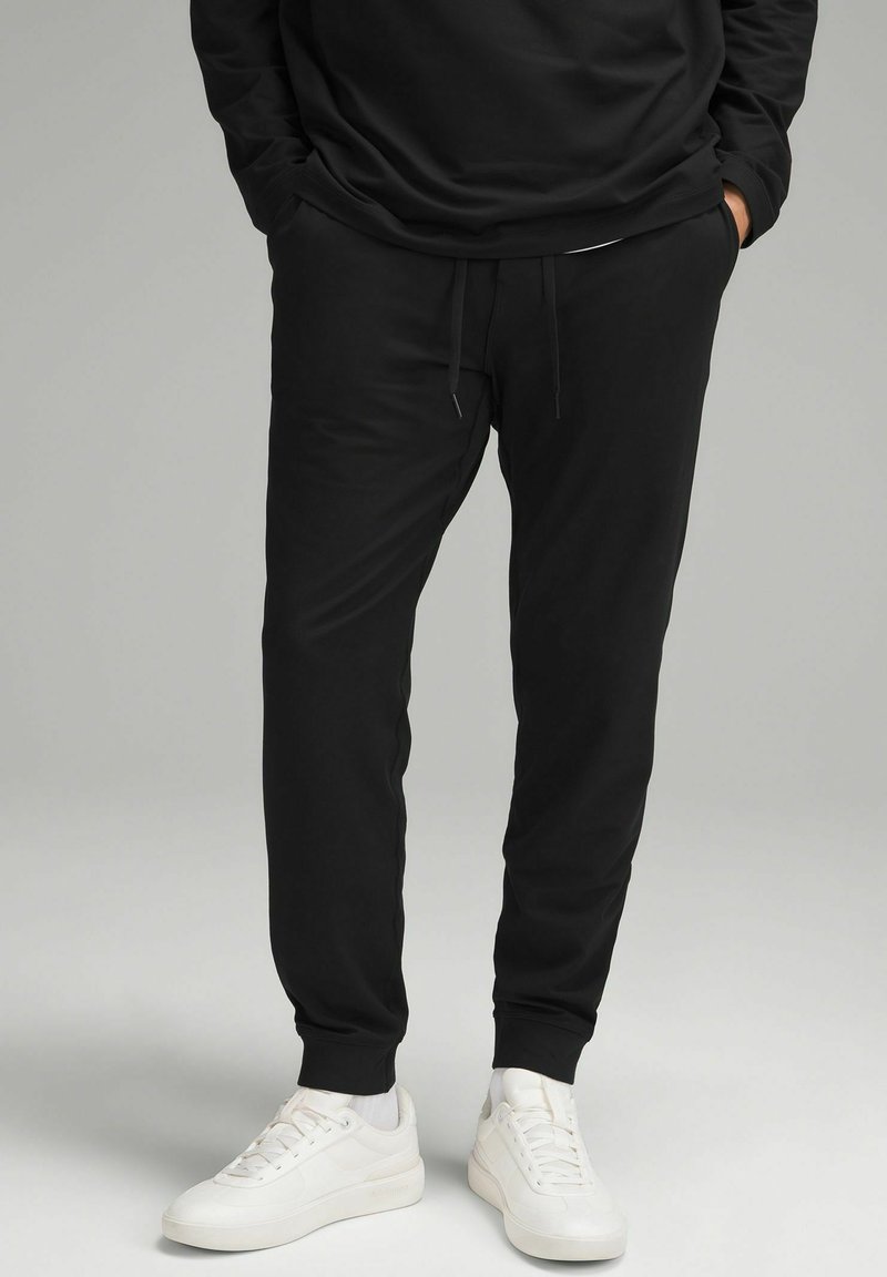 Zwarte katoenen joggers met een elastische tailleband en trekkoord. Tapered leg ontwerp met geribde manchetten, gecombineerd met witte sneakers.