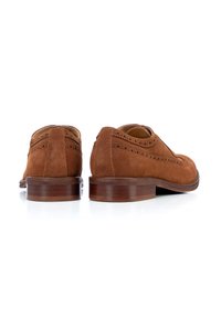 Zapatos de ante marrón con detalles de brogue, puntera redonda y tacón de madera. La vista trasera resalta los bordes suaves y la textura.