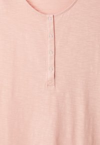 Maglietta henley rosa chiaro realizzata in tessuto morbido, con scollatura arrotondata, cinque bottoni circolari e una texture sottile.