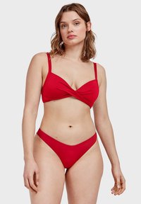 Completo bikini rosso con design intrecciato sulla parte superiore e slip a vita bassa. Tessuto morbido con spalline regolabili e dettagli hardware minimi.