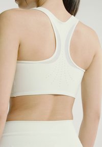 Mujer con un sujetador deportivo blanco con agujeros de ventilación perforados en la espalda, mostrando un primer plano de la parte superior de la espalda y los hombros.