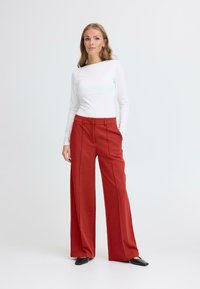 Rode high-waisted wijde broek met een gladde textuur, voorplooien en een tailor-made pasvorm, gecombineerd met een wit top met lange mouwen.