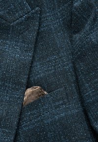 Mörkblå strukturerad blazer med en foderficka, prydd med en inskjuten ljusbrun mönstrad fickduk.