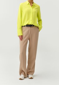 Limegrön randig långärmad skjorta, beige vida byxor, svart bälte med silverspänne, och vita sneakers med ljusbruna sulor.