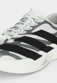 Gros plan d'une chaussure de running blanche et grise avec des rayures noires, des lacets blancs et « LIGHTSTRIKE PRO » sur le bord de la semelle.