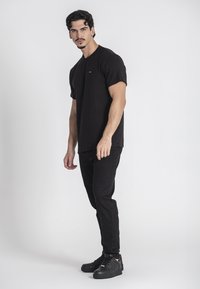 Čierne rebrované tričko s krátkymi rukávmi, v kombinácii s čiernymi slim-fit džínsami a čiernymi teniskami. Jednoduchý dizajn, bez viditeľných log a vzorov.