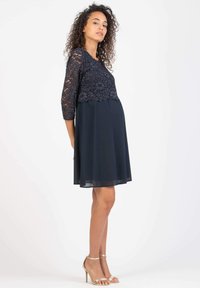 Ein marinefarbenes Kleid mit 3/4-langen Spitzeärmeln, einem Blumenmuster und einem fließenden Chiffonrock, der ein tailliertes Oberteil und eine lockere Taille hat.